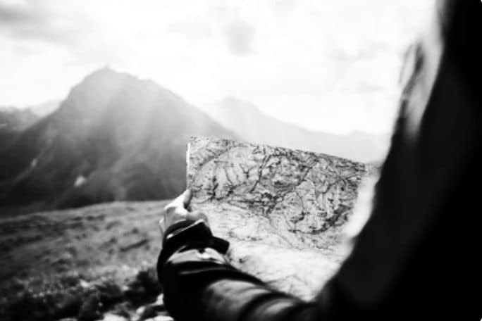 Een hand houdt een kaart vast voor een berglandschap